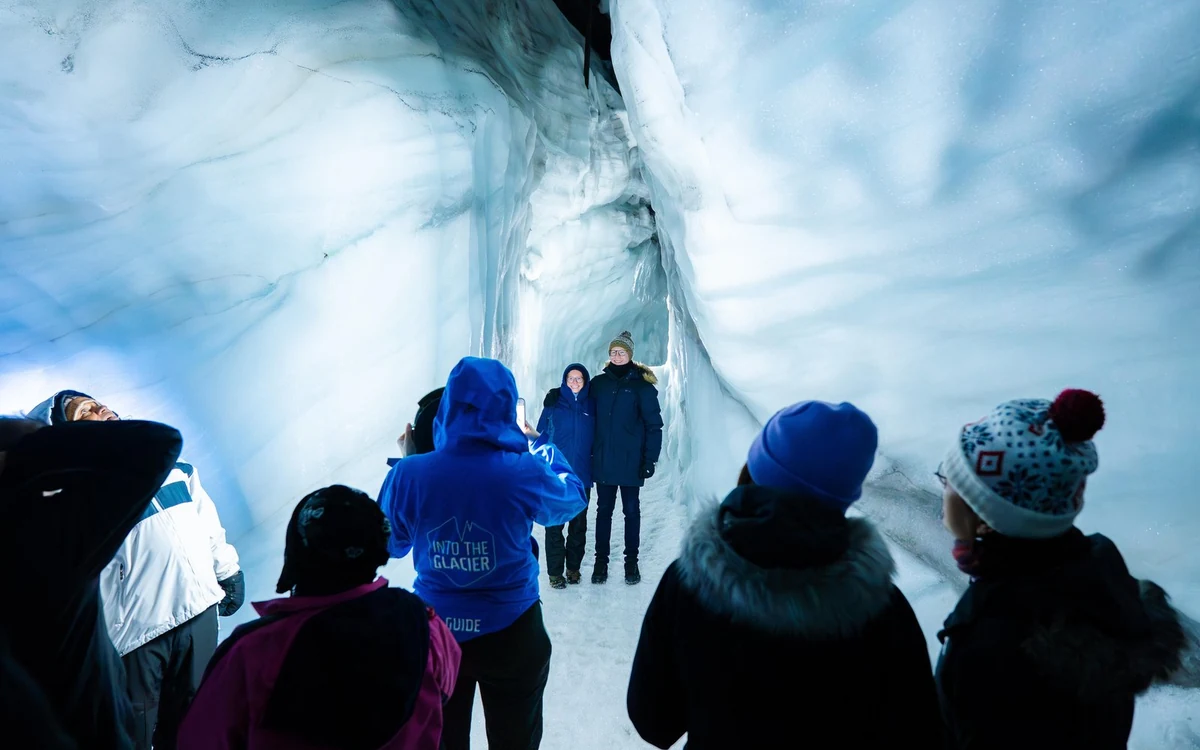 Eine Gruppe von Besuchern in Wintermänteln geht durch einen blauwandigen Tunnel im Inneren des Eisschilds