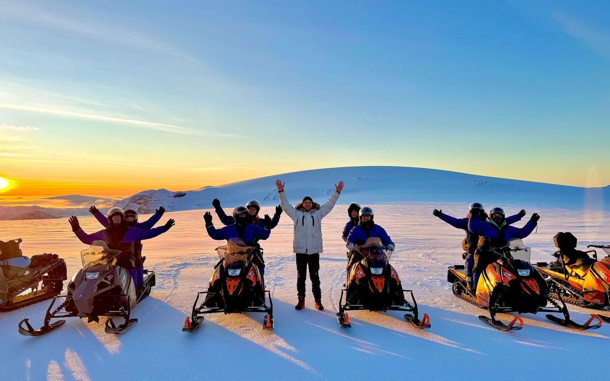 Una fila de conductores de pie junto a sus máquinas sobre el hielo con los brazos levantados al atardecer
