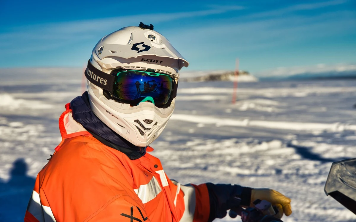 Vista cercana de un conductor con un mono térmico naranja, casco blanco y gafas