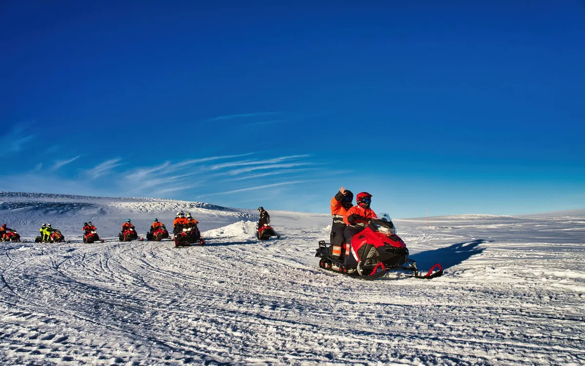 Una fila di motoslitte allineate sulla neve con il bianco della calotta glaciale sullo sfondo