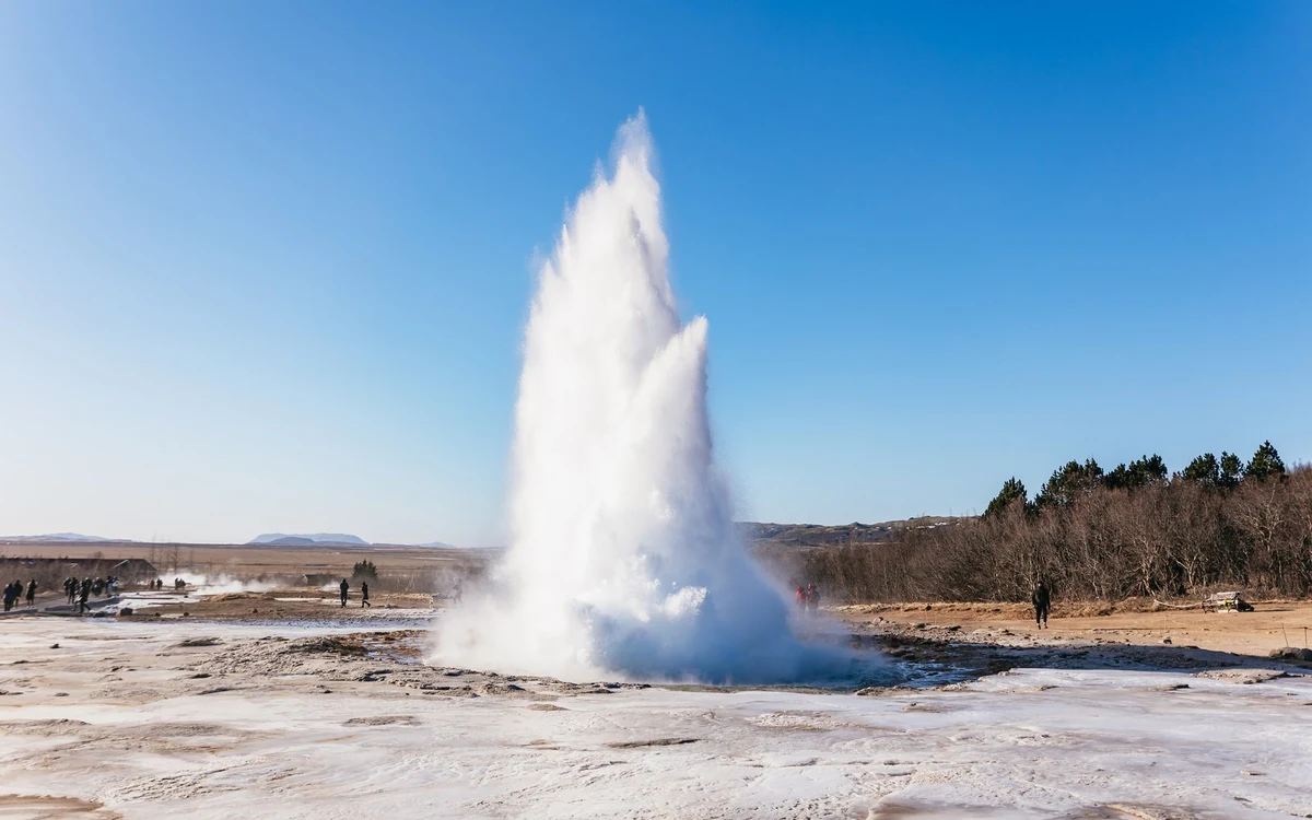 A geyser erupting in a tall white column above a flat brown plain